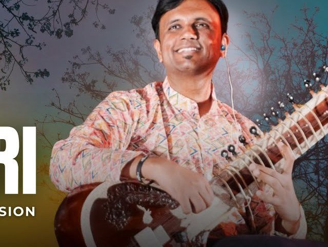 Playing outdoors in white, the sitar across the knee